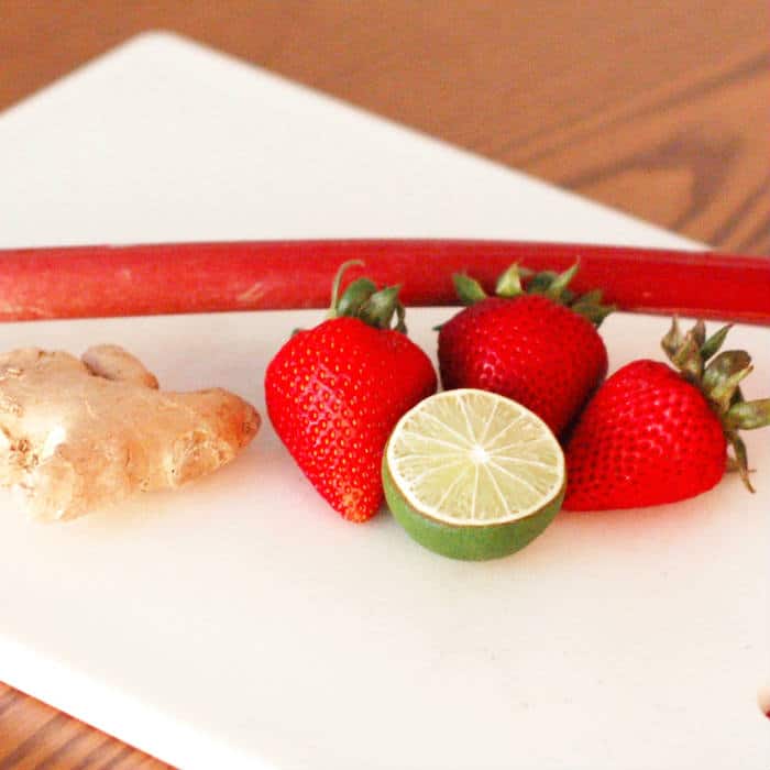 Strawberry rhubarb mimosa ingredients stalk of rhubarb, knob of ginger, strawberries, and a lime on a white cutting board