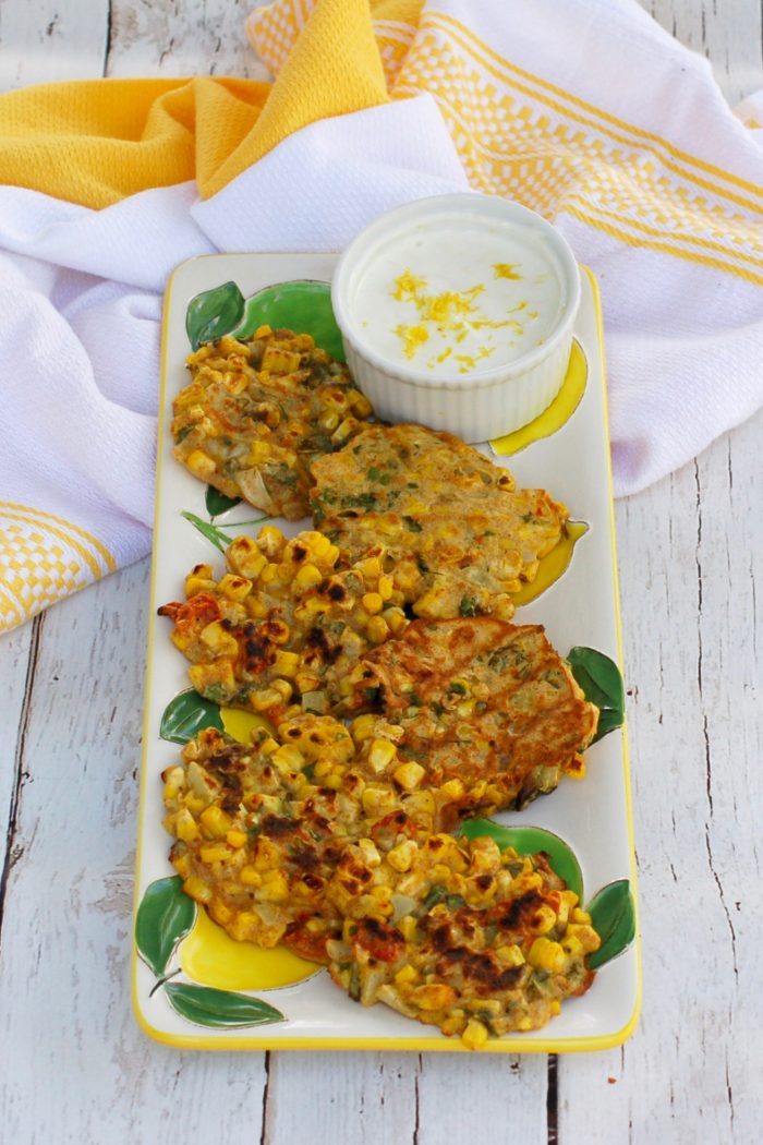 corn and basil cakes overhead picture of Corn & Basil Cakes on serving plate with ramekin of yogurt sauce
