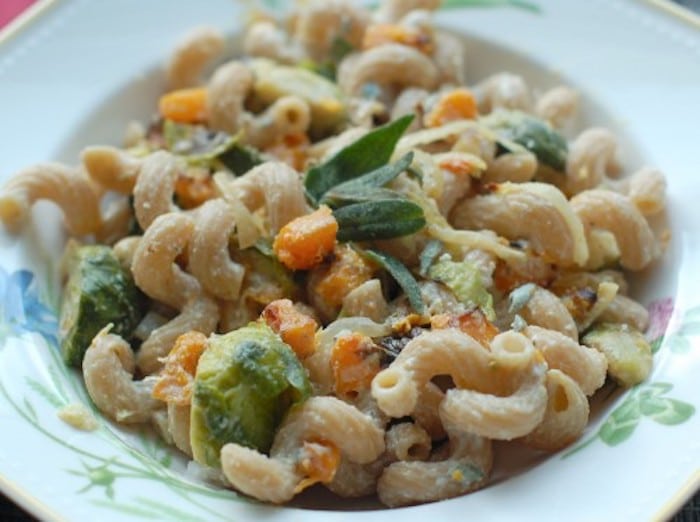 Roasted butternut squash and brussels sprouts tossed with creamy lemon-sage ricotta and a hint of maple syrup make this pasta dish nutritious and delicious, perfect for a cool fall night. Get the full recipe via JessicaLevinson.com #FallPasta #NationalPastaMonth #FallPastaRecipe Roasted Butternut Squash Pasta in White Bowl