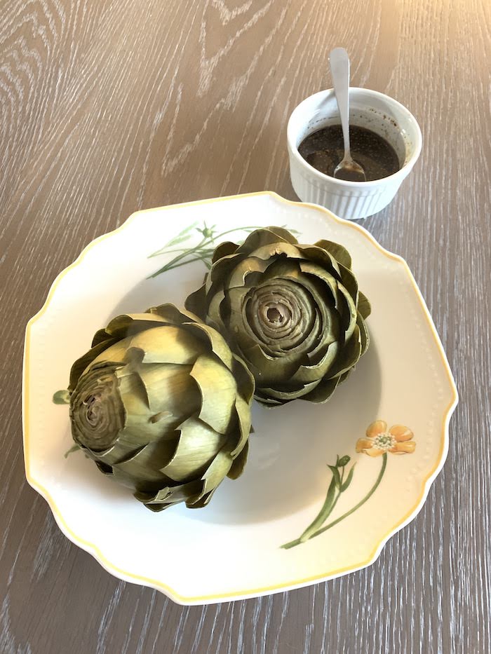 Steamed artichokes are served with a tangy vinaigrette for an irresistible appetizer or side dish. Get the gluten-free and vegan recipe via JessicaLevinson.com #ArtichokesRecipe #InstantPotArtichokes steamed artichokes in bowl with balsamic vinaigrette