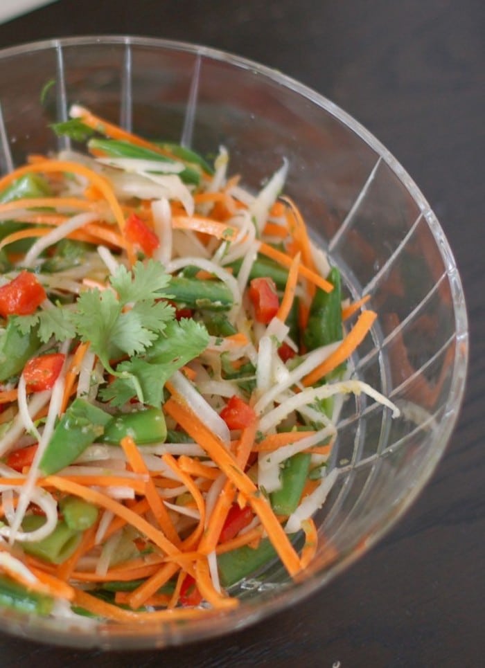 Japanese radish with bright orange carrots, red bell peppers, and snap peas tossed with a Thai citrus dressing make for a quick & easy Thai Citrus Salad Get the full vegan & nut-free recipe via JessicaLevinson.Com #VeganThaiSaladRecipe #EasyThaiSaladRecipe Close Up of Thai Citrus Salad in Clear Bowl