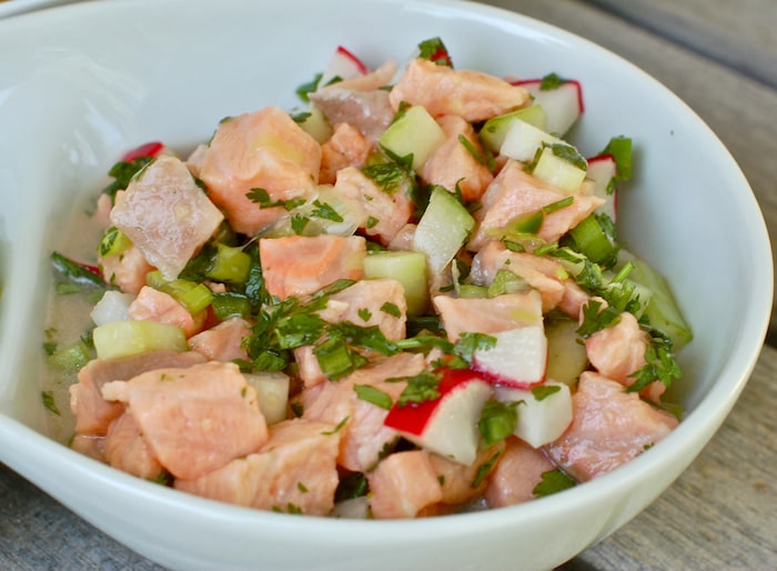 Tender omega-3 rich fish, crunchy vegetables, and a zesty citrus marinade are combined in this easy, recipe-style Salmon Ceviche with Cucumbers and Radishes. Get the gluten-free and dairy-free recipe at JessicaLevinson.com | #ceviche #salmonrecipes Close up of Salmon Ceviche with Cucumbers