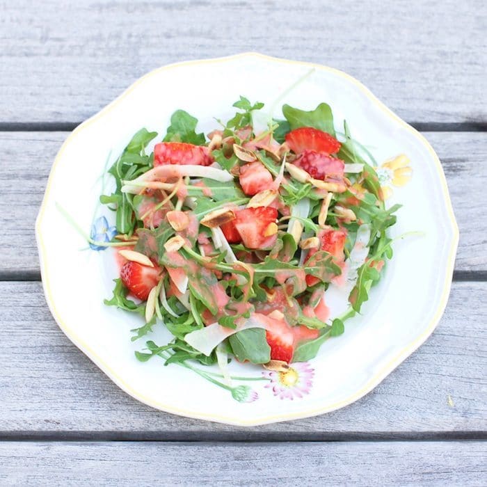 Strawberry Arugula Salad with Fennel, Toasted Almonds, and Strawberry Champagne Vinaigrette is a fresh and sweet salad for the spring and summer. Get the recipe via JessicaLevinson.com #StrawberrySaladRecipe #ArugulaSalad Strawberry Arugula Salad on White Plate
