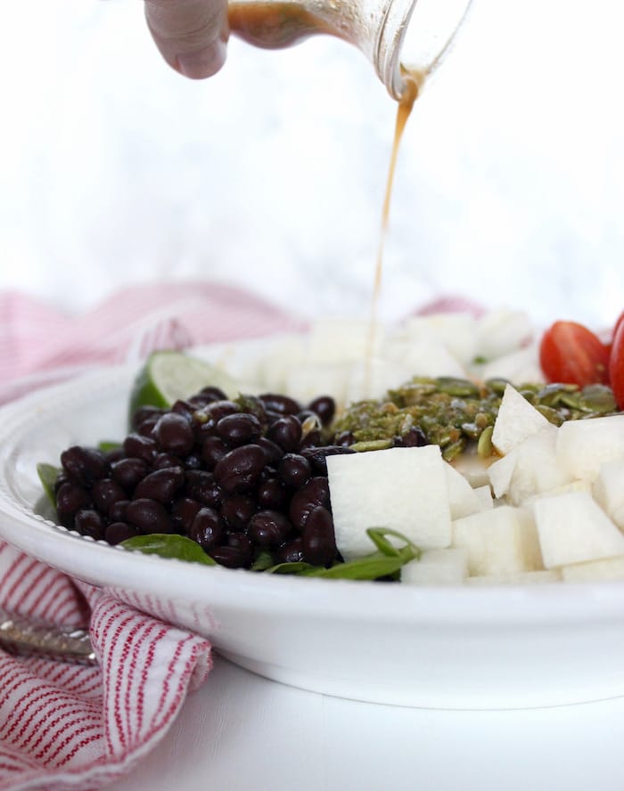 Crisp spinach, crunchy jicama, juicy tomatoes and tender black beans are tossed with a smoky lime vinaigrette in this quick and easy side salad that's the perfect accompaniment to your favorite Mexican-inspired dinner. Vegan, dairy-free, and gluten-free. Get the Spinach Salad with Jicama recipe via JessicaLevinson.com | #SpinachSaladRecipe #JicamaSalad Spinach Salad with Jicama and Salad Dressing Pour