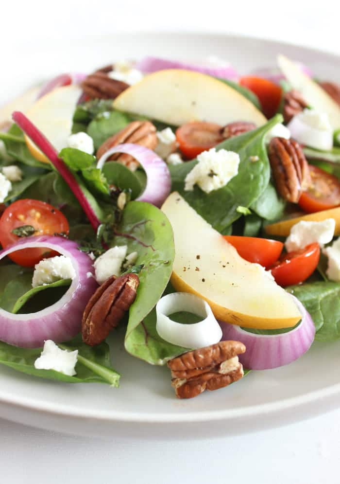 Spinach Pear Salad with Goat Cheese and Lemon Thyme Vinaigrette | There's nothing boring about this flavor-packed salad! A bed of baby spinach is topped with crisp pears, juicy tomatoes, crunchy red onions and pecans, and creamy goat cheese, and tossed in a bright and aromatic lemon thyme vinaigrette. Get the full vegetarian and gluten-free recipe via JessicaLevinson.com #SpinachSaladwithGoatCheese #EasySpinachSalad Close Up of Spinach Pear Salad with Goat Cheese
