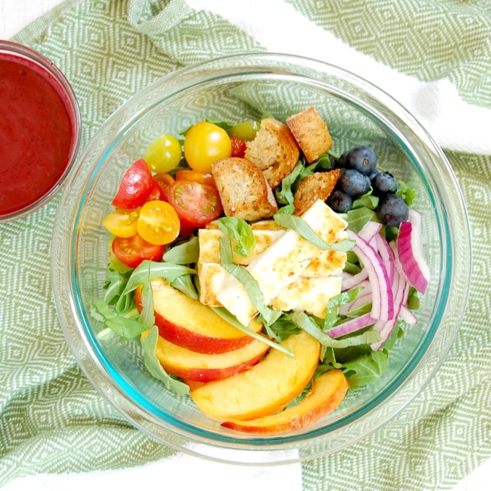 Juicy peaches, ripe tomatoes, briny halloumi cheese, and crunchy rustic bread come together in this Peach Panzanella Salad, a twist on a classic Tuscan summer dish. Get the quick and easy, vegetarian summer recipe at JessicaLevinson.com | #vegetarian #peaches #saladrecipes #summerrecipes bowl of peach panzanella salad tossed with blueberry balsamic dressing