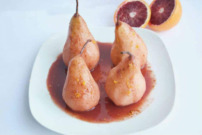 Blood Orange Poached Pears are made with only five simple ingredients, and no added sweeteners. A simple and elegant dessert for any occasion! Get the vegan and gluten-free recipe at JessicaLevinson.com | #lowsugar #winterrecipes #oranges #pears Blood Orange Poached Pears on White Plate
