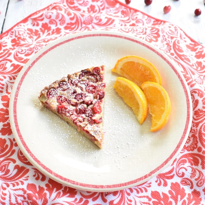 slice of cranberry orange dutch baby slice of cranberry dutch baby on plate with sliced oranges