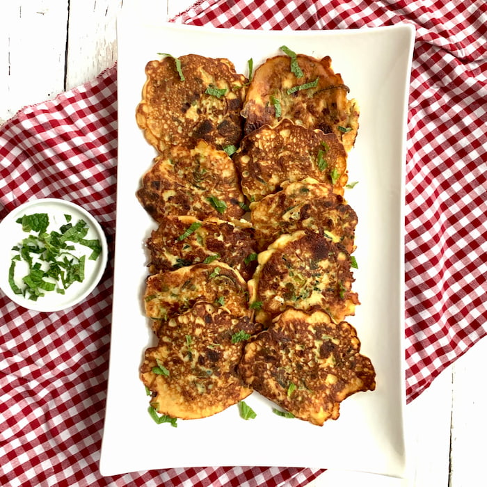 serving platter of zucchini pancakes zucchini pancakes on white serving platter with side ramekin of yogurt sauce